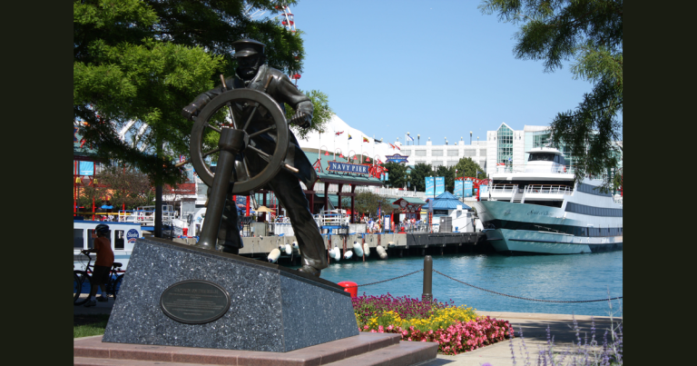 Navy Pier 海滨的掌舵人物雕像、码头与船只，背景可见海军码头入口标识